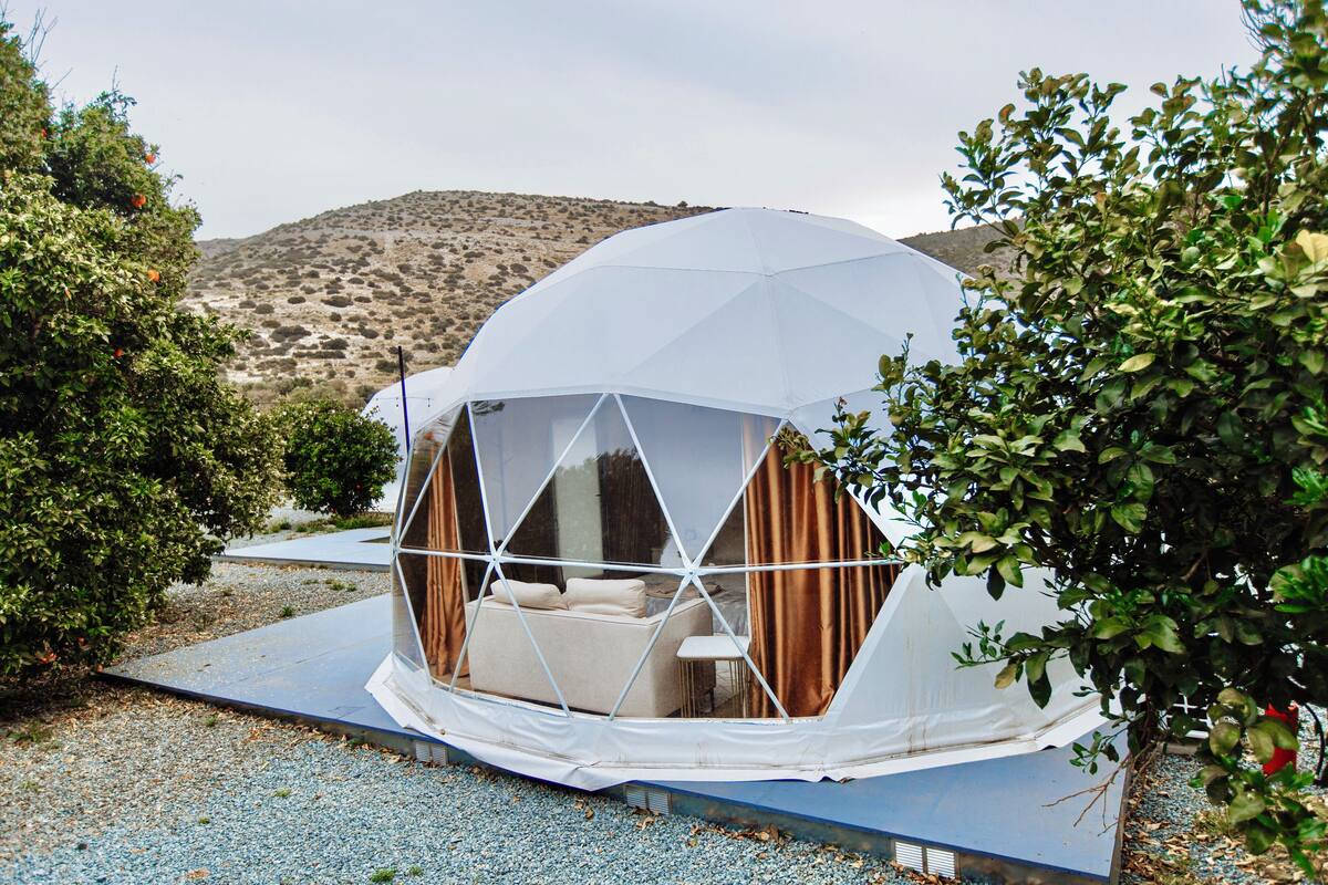 A dome-shaped tent with a sofa and curtains, surrounded by gravel and greenery.