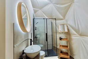 Un baño moderno con cabina de ducha de vidrio, un lavamanos blanco y una repisa de madera.