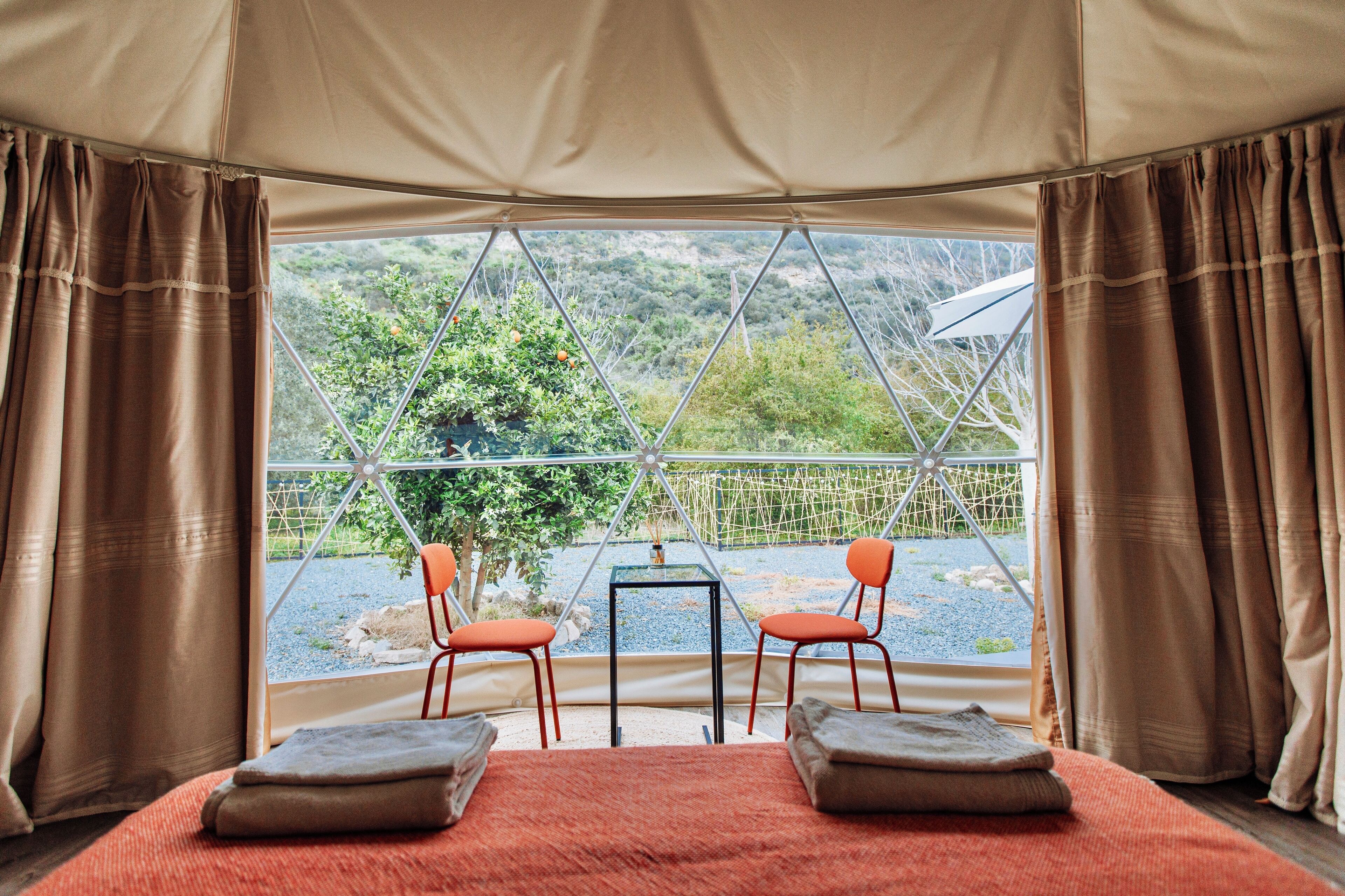 A tented room with a bed, two chairs, and a table.