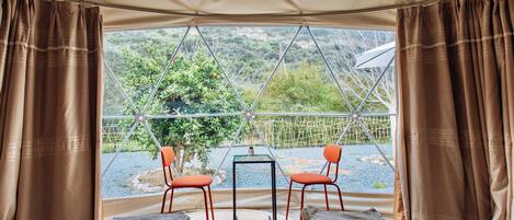 A tented room with a bed, two chairs, and a table.
