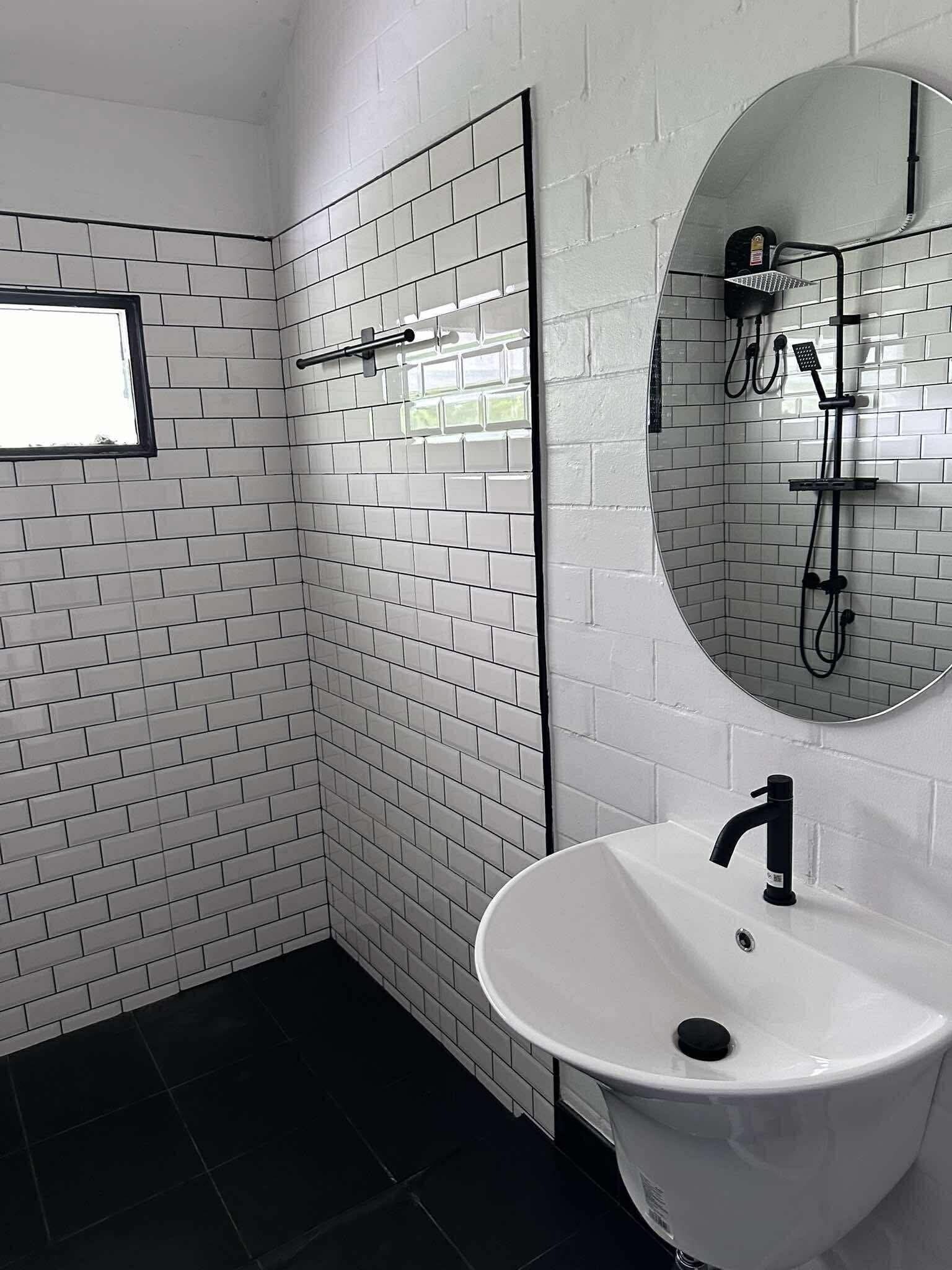A bathroom with white subway tiles, a white sink with a black faucet, a shower with a handheld showerhead, and a mirror above the sink.