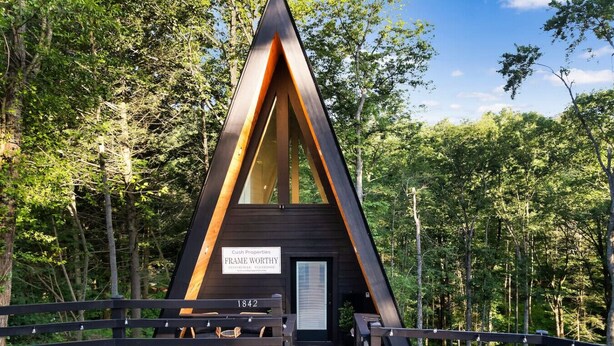 Een moderne, driehoekige houten cabin met een bord waarop staat: Cush Properties FRAME WORTHY.