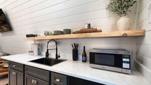 A kitchen with a sink, a microwave, and a shelf above the counter. - Frame Worthy - Luxe A-Frame, Treehouse, Hot Tub, Sauna (Sevierville)