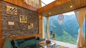 Ein gemütliches Wohnzimmer mit Steinwand, einem grünen Sofa und einem großen Fenster mit Bergblick.