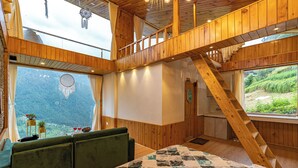 Ein Holzinnenraum mit einem Bett, einer Treppe und Blick auf eine gebirgige Landschaft.