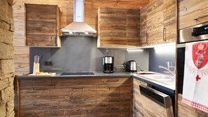 A compact kitchen with wooden cabinetry, a stainless steel range hood, a coffee maker, and a refrigerator with a red and white design. - Chalet Leßner - Pure design & tranquility (Leutasch)