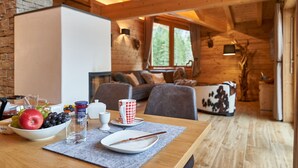 A wooden interior with a dining table set with fruits, a bowl, and a cup. There is a sofa and a fireplace in the background. - Chalet Leßner - Pure design & tranquility (Leutasch)