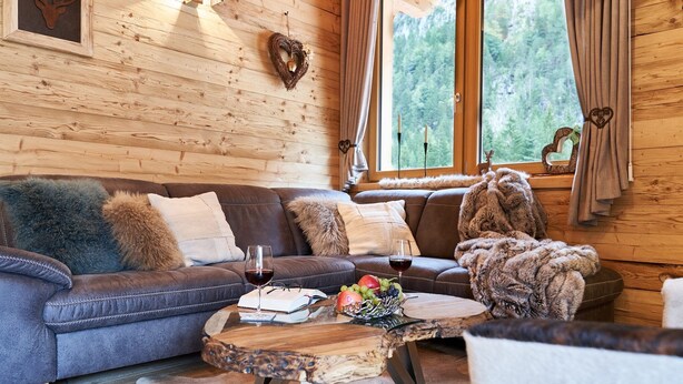 A cozy cabin interior with a wooden log wall, a brown leather sofa, a round coffee table with a book and glasses, and a fruit bowl. - Chalet Leßner - Pure design & tranquility (Leutasch)