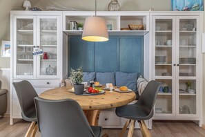 A dining area with a round wooden table, four chairs, a hanging light fixture, and a blue cushioned bench.