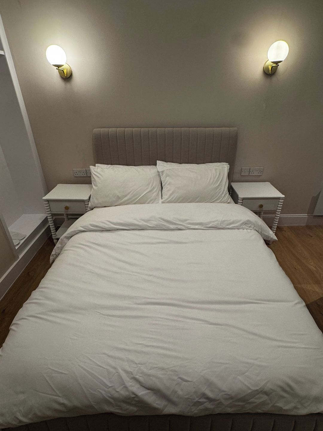 Un lit avec une literie blanche, deux tables de chevet et des lampes fixées au mur.