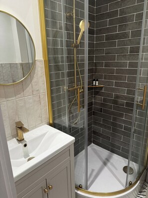 A bathroom with a white sink, a mirror, a shower with a glass door, and a tiled wall.