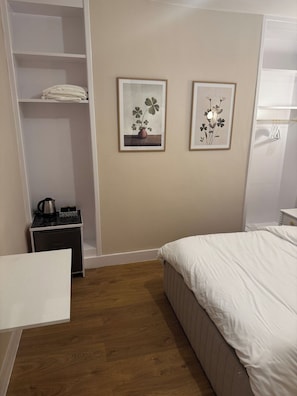 Ein Schlafzimmer mit einem Bett, einem Nachttisch mit Wasserkocher und zwei gerahmten Bildern an der Wand.