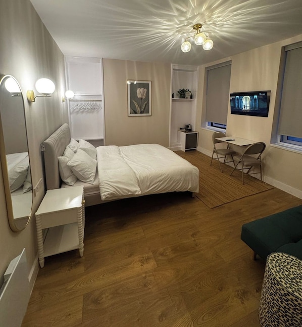 A bedroom with a bed, bedside table, mirror, wall-mounted TV, and a desk with a chair.