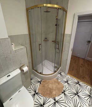 A shower with a glass door, a toilet, and a patterned floor. - Peckham Haven (Greater London)