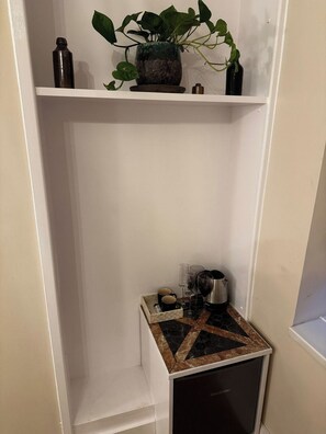 A small kitchenette with a countertop, a trash bin, and a potted plant on a shelf. - Peckham Haven (Greater London)