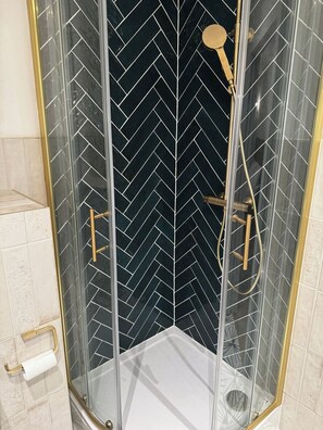A glass-enclosed shower with a black and white herringbone tile pattern, gold fixtures, and a clear glass door. - Central Peckham Studio Retreat (Greater London)