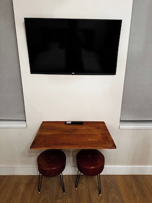 A flat-screen TV mounted on a wall above a wooden table with two red stools.