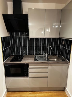 A compact kitchen with a black range hood, a built-in dishwasher, a sink, and white cabinets.