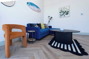 Ein modernes Wohnzimmer mit einem blauen Sofa, einem orangefarbenen Sessel, einem kleinen runden Tisch und einem schwarz-weißen Teppich.