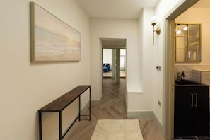 A hallway with a wooden floor, a bench, a painting, and a kitchen area with a sink and cabinets.
