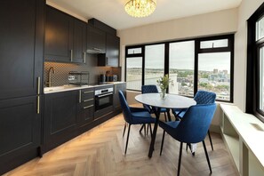 A modern kitchen with dark cabinetry, a built-in oven, and a dining area with a round table and blue chairs.
