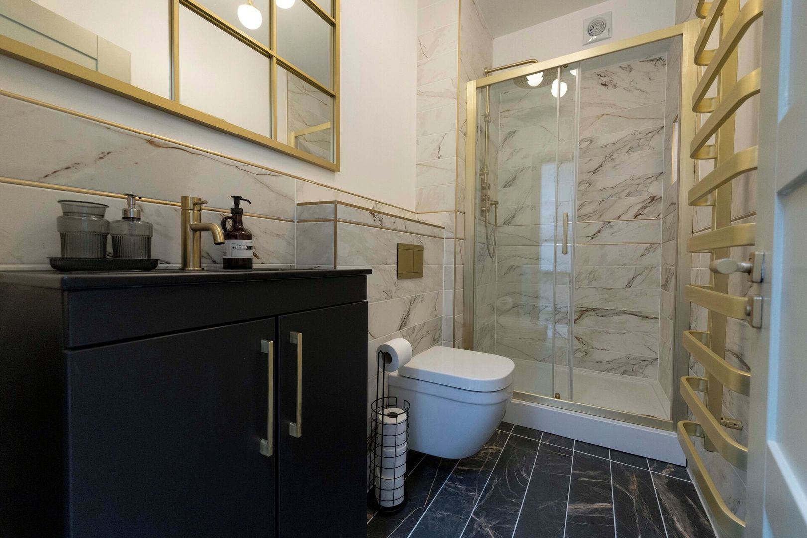 Un bagno moderno con cabina doccia in marmo, un mobile lavabo nero e un water.