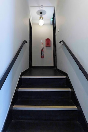 Eine Treppe mit schwarzen Stufen und weißen Wänden, ein Feuerlöscher und eine Leuchte.