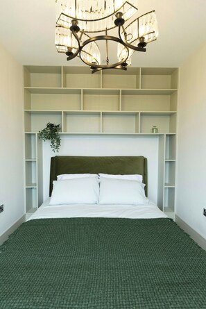 A bedroom with a bed, a headboard, a chandelier, and built-in shelving.