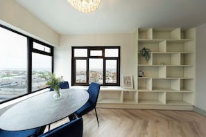 A modern dining area with a round table, blue chairs, a vase with greenery, and a city view through large windows.