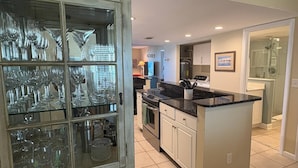 A modern kitchen with a central island, built-in appliances, and a glass-fronted cabinet displaying various glassware. - Windjammer 115 (St. Augustine)
