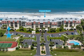 A multi-story hotel with a parking lot, a tennis court, and a pool.