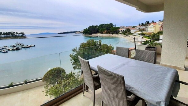 A balcony with a table and chairs overlooking a coastal area with boats and a beach.
