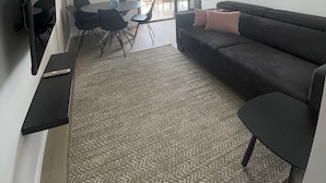 A modern living room with a sofa, TV, dining area, and a large window.