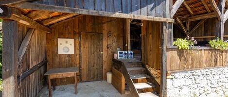 A rustic wooden building with a porch, a toilet, and a small table.