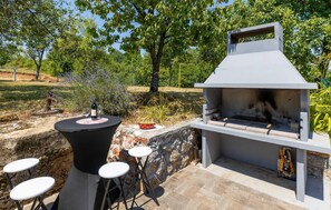 Un espace barbecue extérieur avec un mur en pierre, un gril et une table ronde entourée de tabourets.