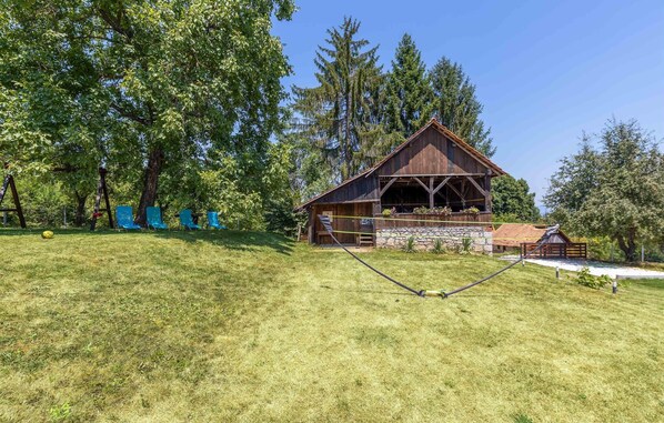Une cabane en bois rustique, posée sur des fondations en pierre, entourée d’une végétation luxuriante et de grands arbres.