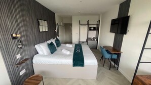 A modern hotel room with a large bed, a desk, a TV, and a wardrobe.