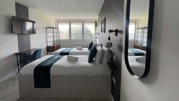 A modern hotel room with two beds, a TV, a desk, and a large mirror.