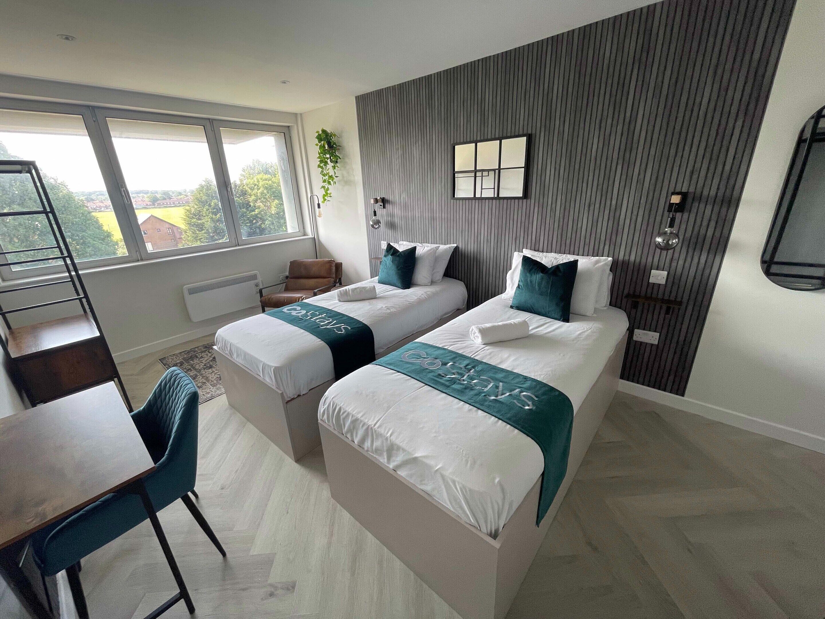 Een moderne hotelkamer met twee bedden, een bureau en een groot raam.