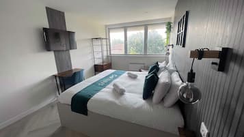 Una habitació d'hotel moderna amb un llit gran, un televisor fixat a la paret i una finestra amb vista a arbres.