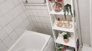 A bathroom with a white bathtub, a shelf with toiletries, and a shower area. - Charming Victorian Apartment in Central Wolverhampton (Wolverhampton)