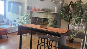 A modern living room with a wooden table, two bar stools, a fireplace, and various decorative items. - Charming Victorian Apartment in Central Wolverhampton (Wolverhampton)