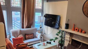 A living room with a sofa, a coffee table, a TV, and a fireplace. - Charming Victorian Apartment in Central Wolverhampton (Wolverhampton)