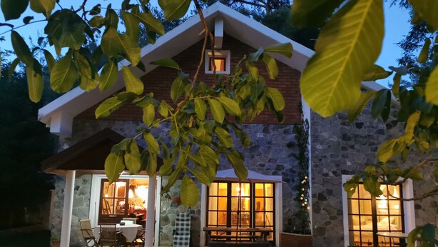 Una casa de piedra con un patio, una zona de comedor con sillas y una mesa, y un banco.