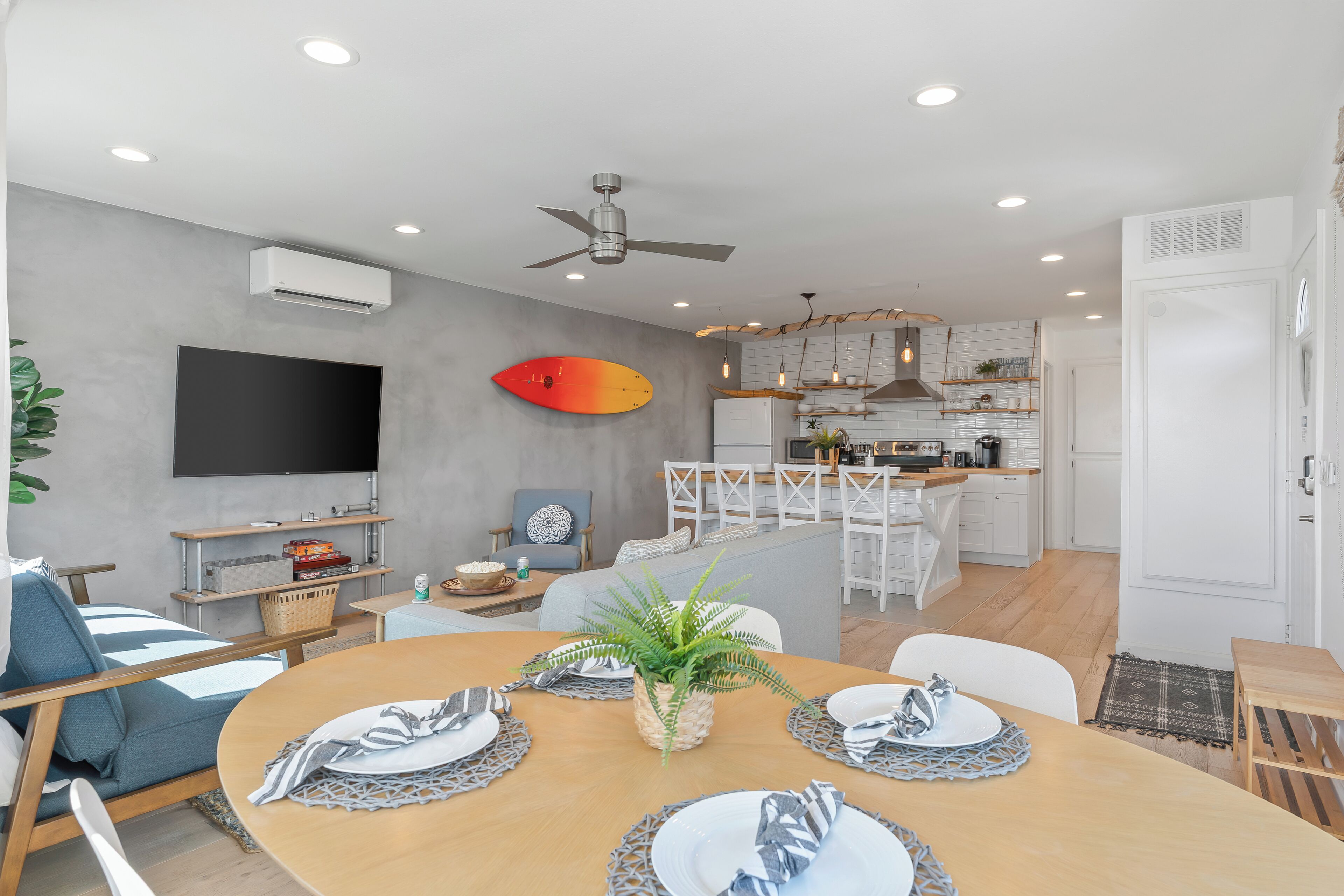 A modern living room with a dining area, a kitchen, and a TV mounted on the wall.