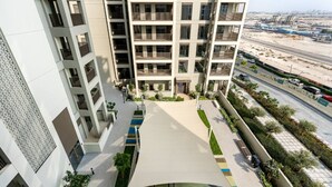 Un immeuble résidentiel à plusieurs étages doté de balcons, d’un espace extérieur couvert agrémenté de verdure et offrant une vue sur une autoroute et une zone industrielle.