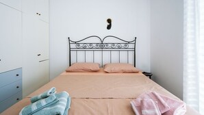 Ein ordentlich gemachtes Bett mit Metallkopfteil, zwei Kissen und einem Paar gefalteter Handtücher an der Seite.