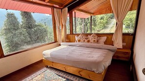 Une chambre située dans un chalet en bois, avec un grand lit, une vue sur les arbres et un auvent rouge.