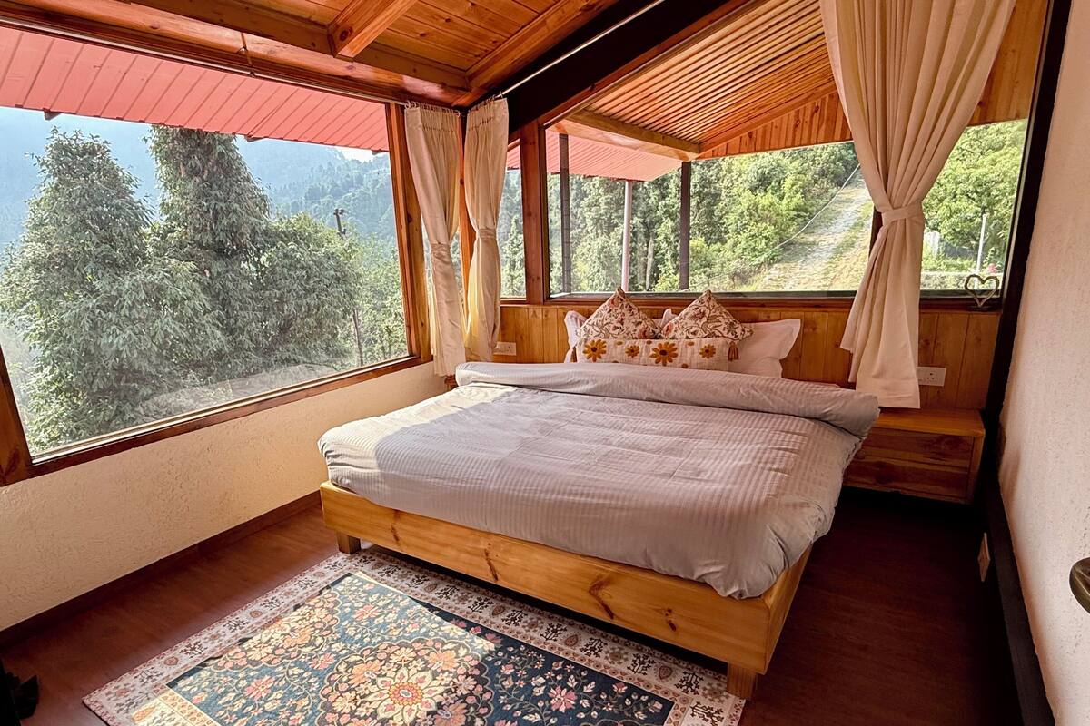 Une chambre située dans un chalet en bois, avec un grand lit, une vue sur les arbres et un auvent rouge.