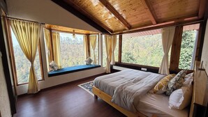 Une chambre avec un lit en bois, un coin fenêtre agrémenté de rideaux et une vue sur une zone boisée.